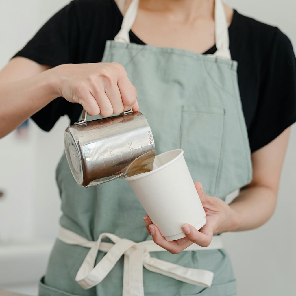 A barista gracefully pours fresh coffee into a paper cup, showcasing beverage preparation art.