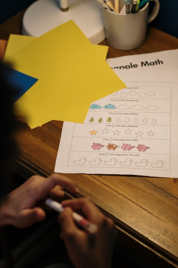 A child working on a simple math worksheet with colorful paper on a wooden desk.
